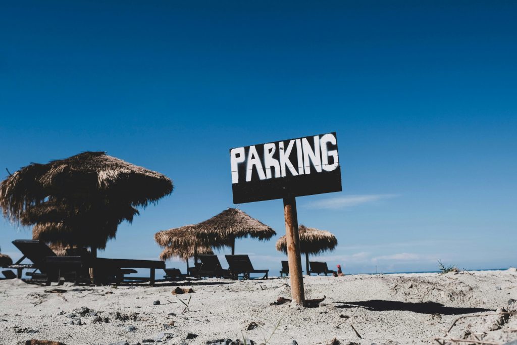 A serene beach scene with a parking sign and straw huts under a clear blue sky.